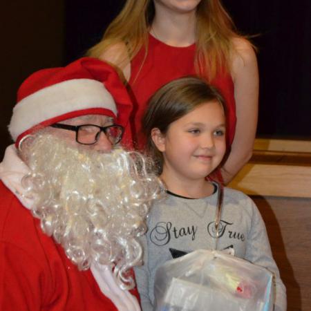 Mikołaj ze śnieżynką pozuje do zdjęcia z dziewczynką z prezentem