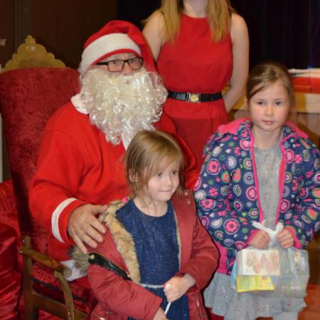 Mikołaj ze Śnieżynką trzyma dzieci z prezentami na kolanach