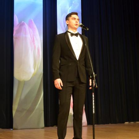 Młody mężczyzna w garniturze śpiewa do mikrofonu na scenie w RCK