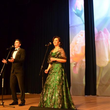 Trzech mężczyzn i kobieta w zielonej sukni śpiewają na scenie przy mikrofonach