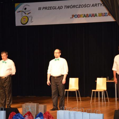 Trzech mężczyzn w garniturach stoją na scenie
