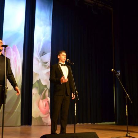 Trzej mężczyźni spiewają na scenie przy mikrofonach