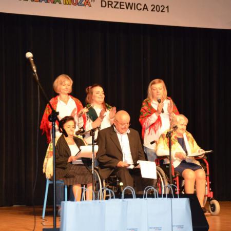 Trzy osoby na wózkach inwalidzkich występują na scenie, za nimi stoją trzy kobiety.